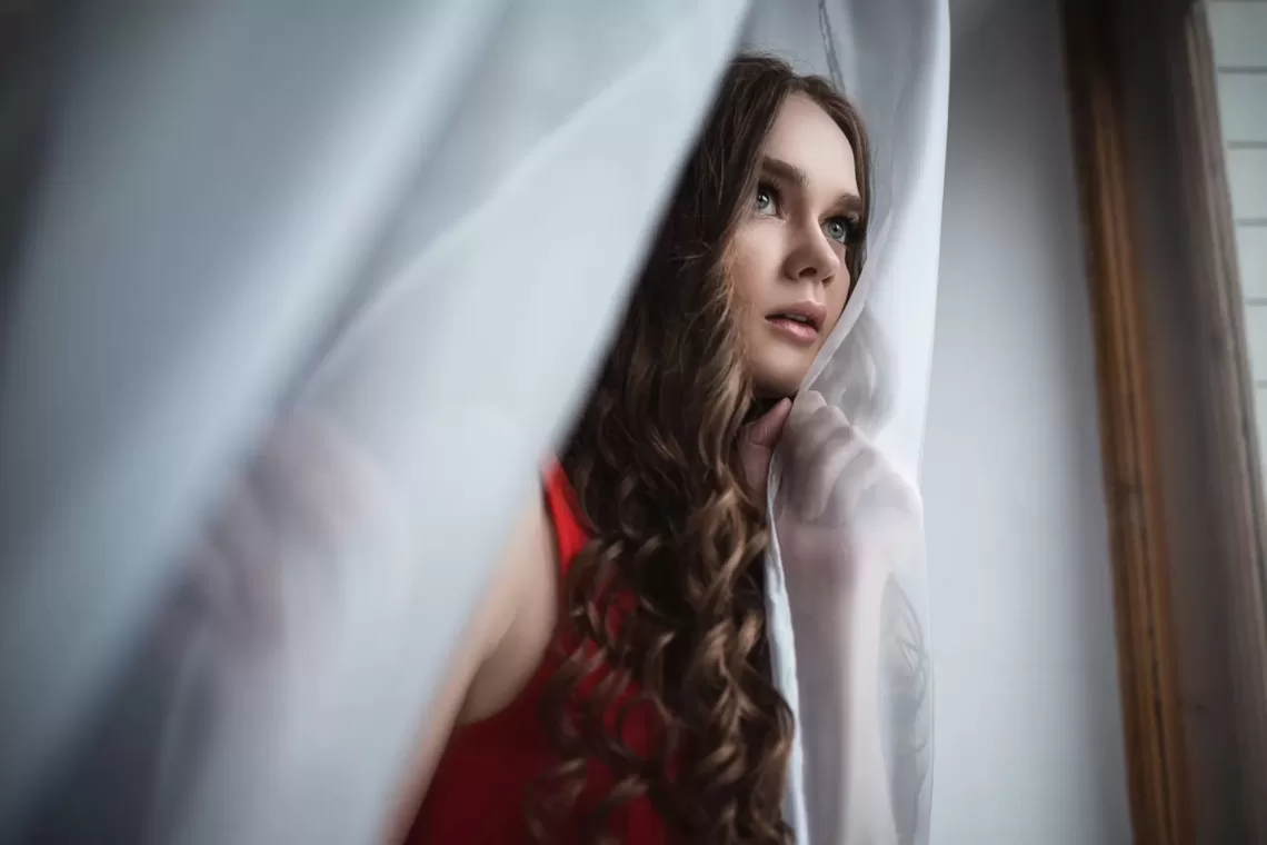 woman on a red dress peeking through curtains